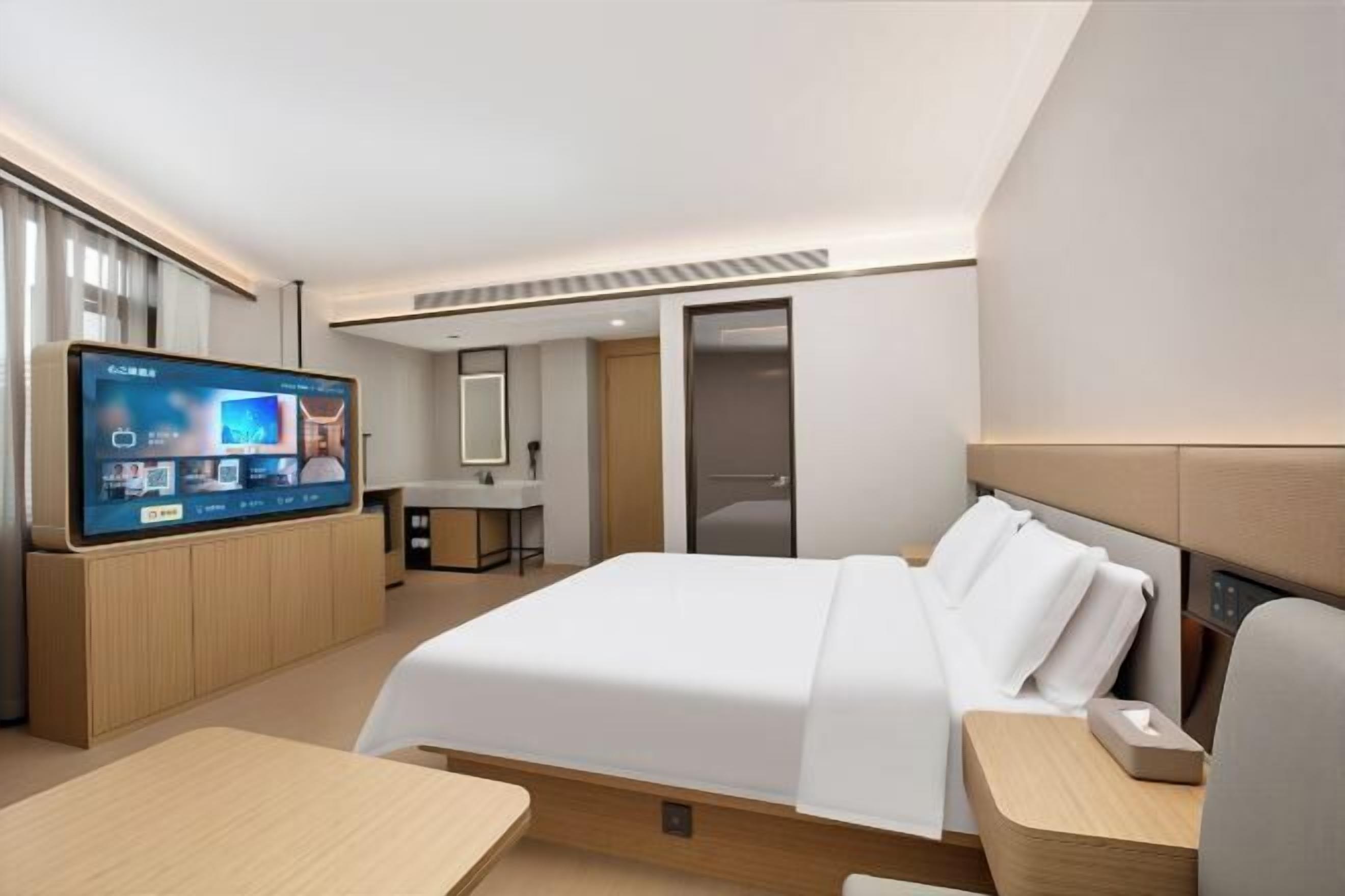 Une chambre d’hôtel moderne équipée d’un lit, d’une table de chevet, d’une télévision et d’un espace bureau.