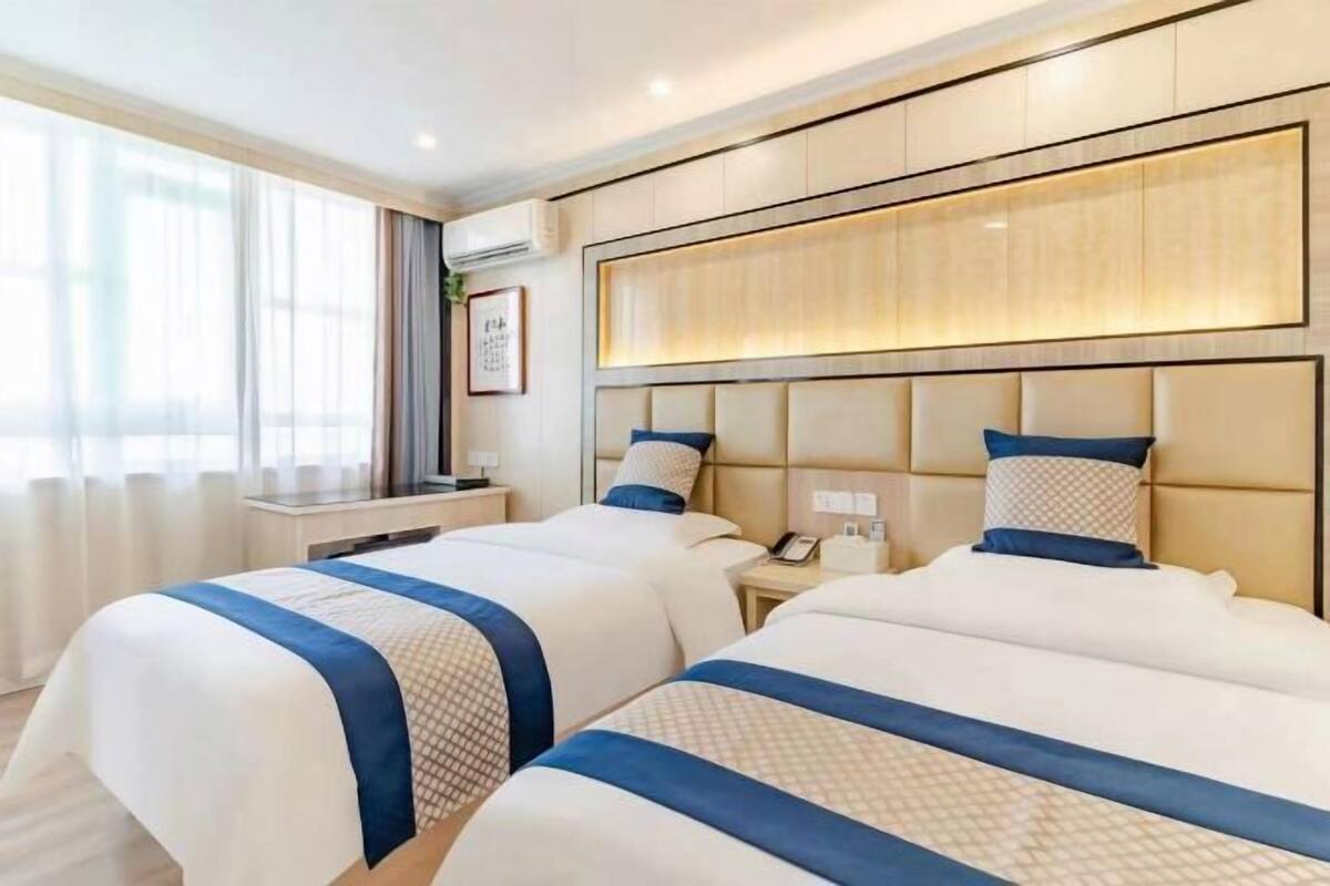Habitació d'hotel amb dos llits, una taula de nit i una finestra gran amb cortines.