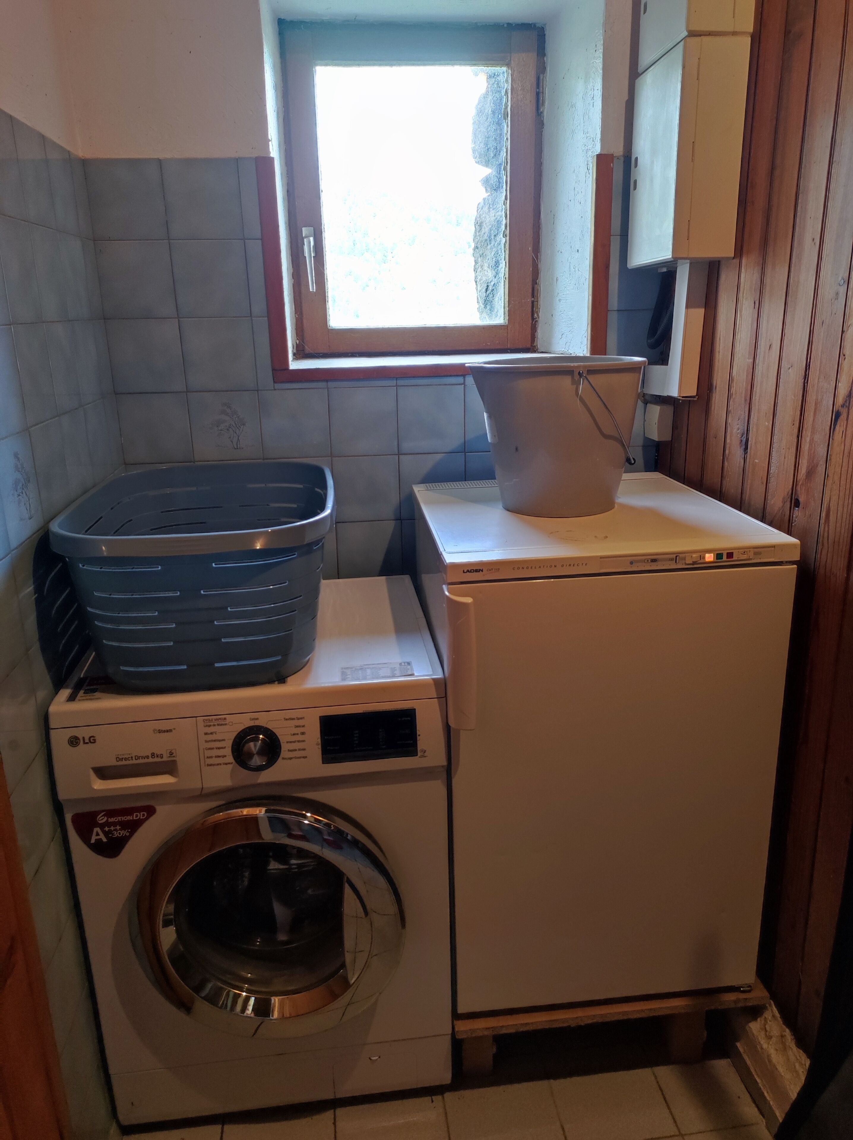 Un espace buanderie compact comprenant un lave-linge, un sèche-linge et une fenêtre située au-dessus.