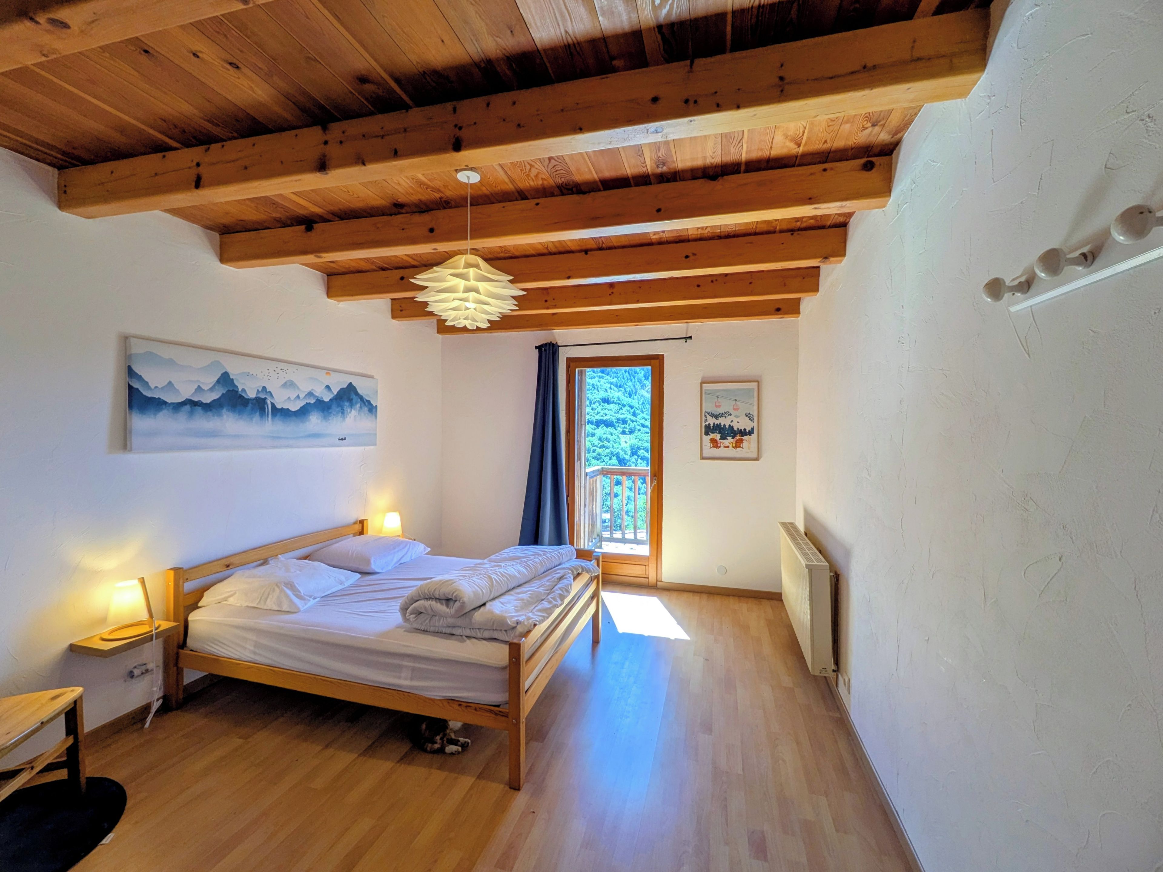 Une chambre avec un plafond en bois, un lit, une table de chevet, un radiateur et une fenêtre donnant sur un paysage verdoyant.