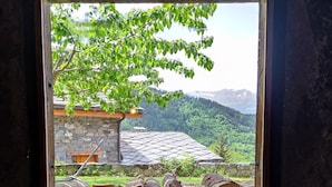 A window with a view of a stone building, a tree, and a stack of logs.