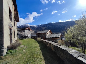 Edificio in pietra tradizionale con balcone, muro in pietra e vista sulle montagne innevate.