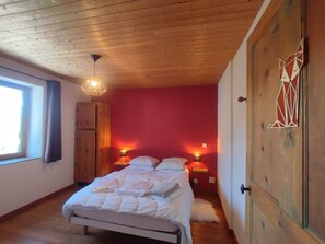 A bedroom with a wooden ceiling, a bed with white bedding, two bedside lamps, and a window with curtains.