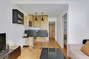 Eine moderne Wohnung mit Küche, zwei schwarzen Stühlen, einem Sofa und einem Fernseher.