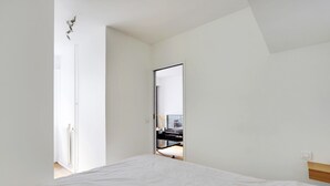 Une chambre à coucher avec un lit, un grand miroir et une vue sur un espace de vie comprenant un téléviseur et un bureau.