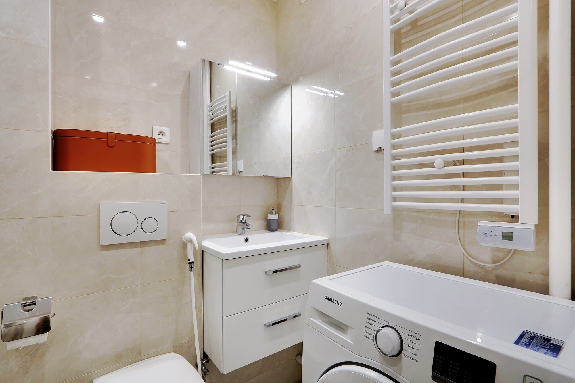 Une salle de bain moderne avec un lavabo blanc, un miroir et un lave-linge Samsung.