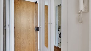 Une porte en bois dotée d’un système coulissant, un téléphone blanc fixé au mur et le reflet d’un lave-linge.
