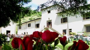A white building with multiple windows and a balcony, surrounded by greenery and outdoor seating. - Villa Grassina (Pelago)