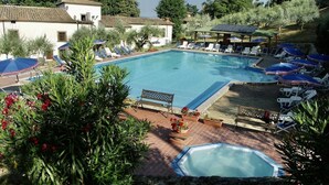 A pool area with lounge chairs and umbrellas, surrounded by greenery and buildings. - Villa Grassina (Pelago)