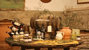 A rustic table with various bottles of wine, a large wooden barrel, and a rustic setting with stone walls and a framed picture. - Villa Grassina (Pelago)
