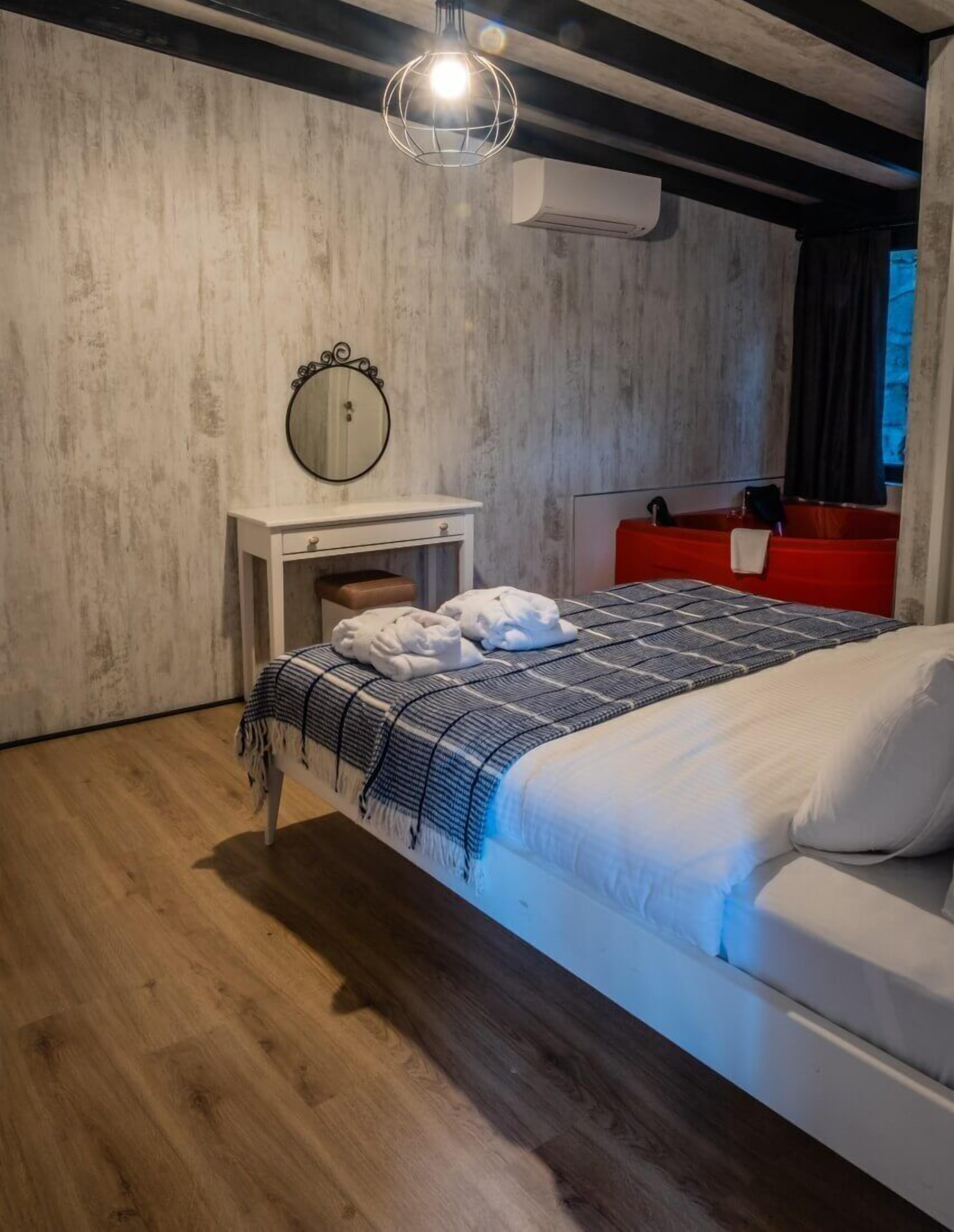 Een moderne slaapkamer met een houten vloer, een bed met witte beddengoed, een rode nachtkastje, een ronde spiegel en een hangende lamp.
