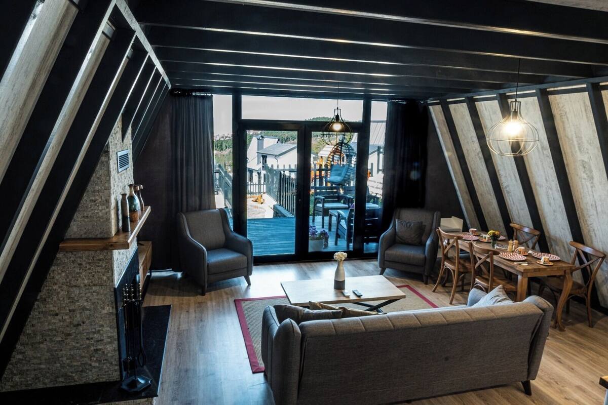 Ein stilvolles Loftzimmer mit Essbereich, zwei Sesseln, einer Couch und einem großen Fenster mit Blick auf eine Stadtlandschaft.