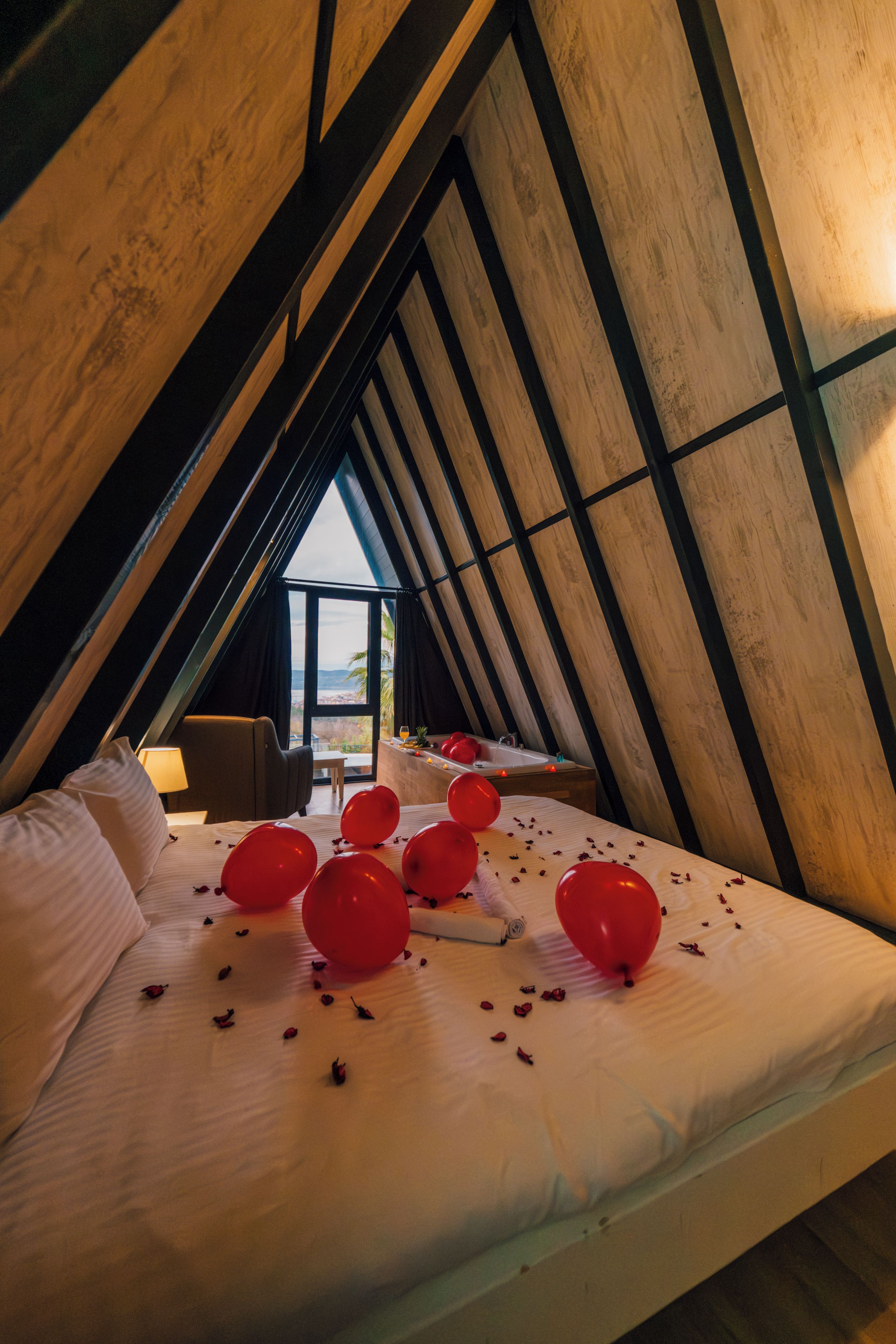 Une chambre avec un plafond en pente, un lit décoré de ballons rouges et une vue par la fenêtre.