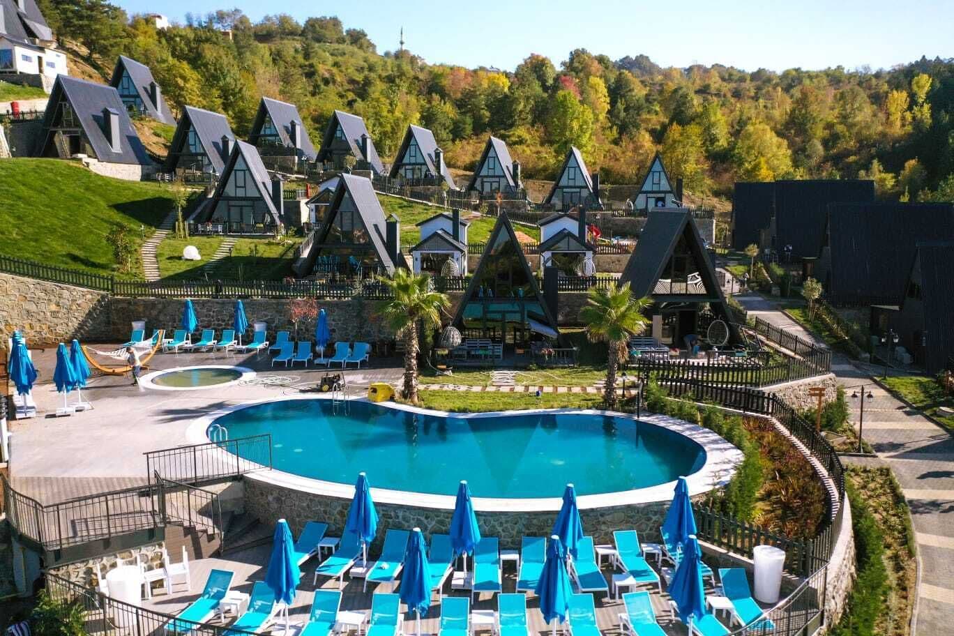 A resort with multiple chalet-style buildings, a central swimming pool with sun loungers, and a landscaped garden.