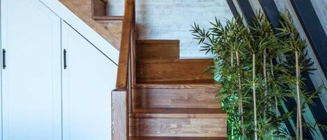 A wooden staircase with a clock on the wall and a bamboo plant beside it.
