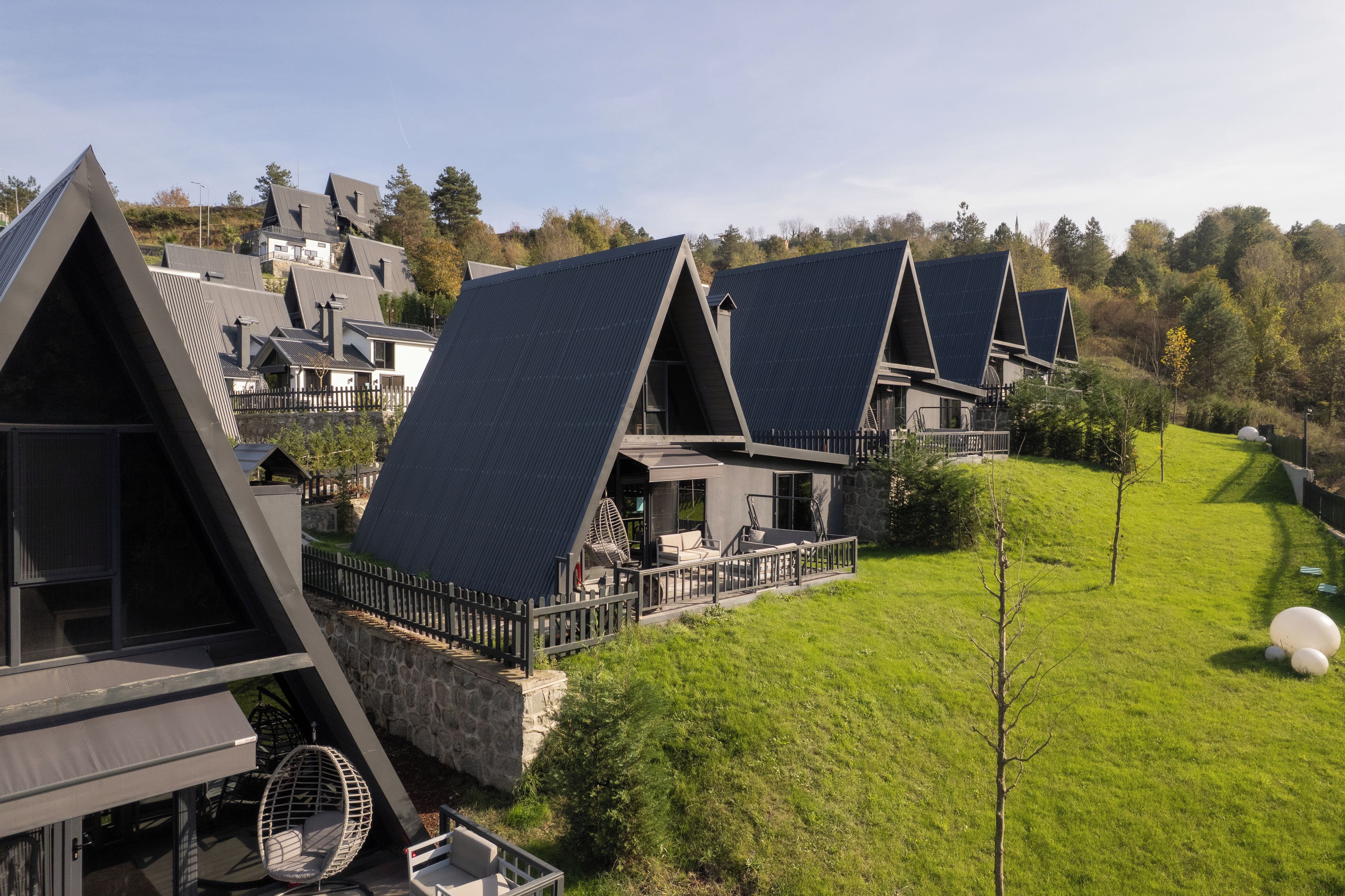 A row of modern, triangular-roofed cabins with outdoor seating areas, set in a lush green landscape.