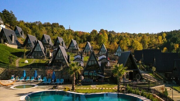 Een resort met meerdere gebouwen in chaletstijl, een zwembad en een heuvelachtige achtergrond.