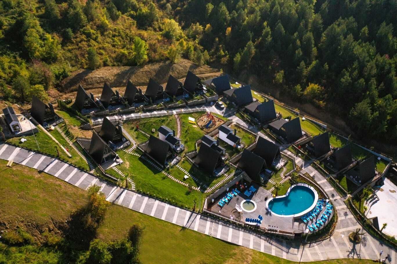 An aerial view of a resort with multiple bungalow-style accommodations, a central pool area, and surrounding greenery.
