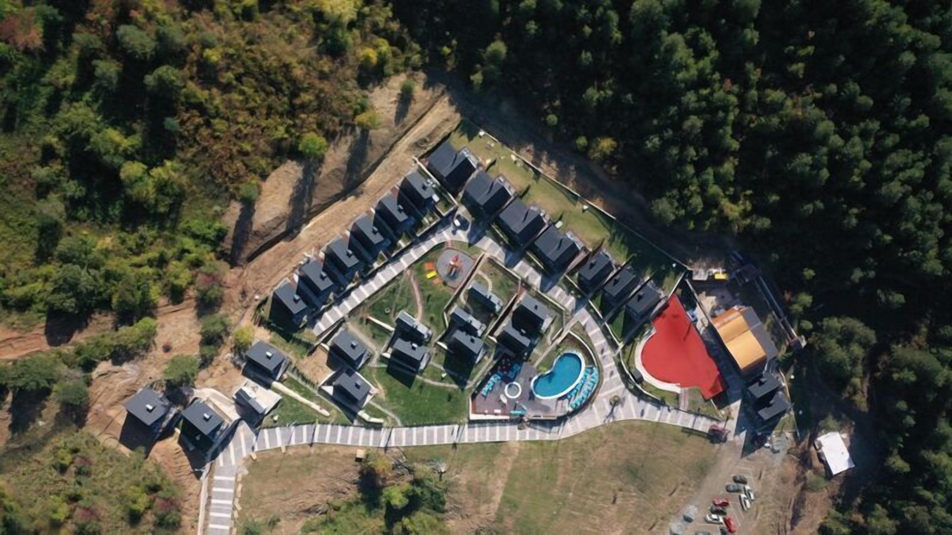 An aerial view of a residential area with multiple houses, a swimming pool, and a fenced playground.