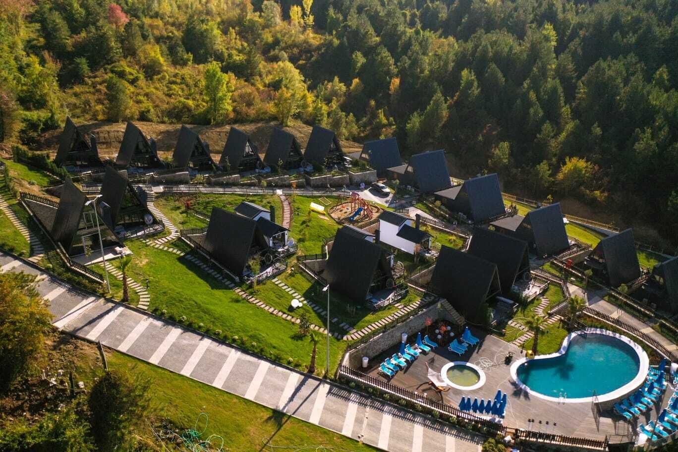 An aerial view of a resort with multiple bungalow-style accommodations, a central pool area, and surrounding greenery.