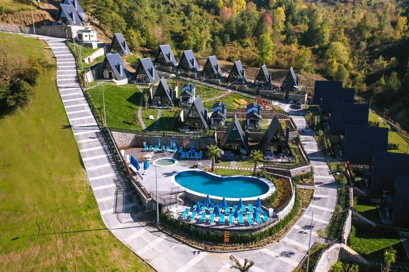 An aerial view of a resort with multiple villas, a central swimming pool, and a well-maintained landscape.