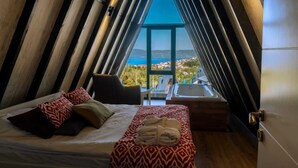 Een slaapkamer met een bed, een stoel, een kleine tafel en een badkuip, allemaal met uitzicht op zee.