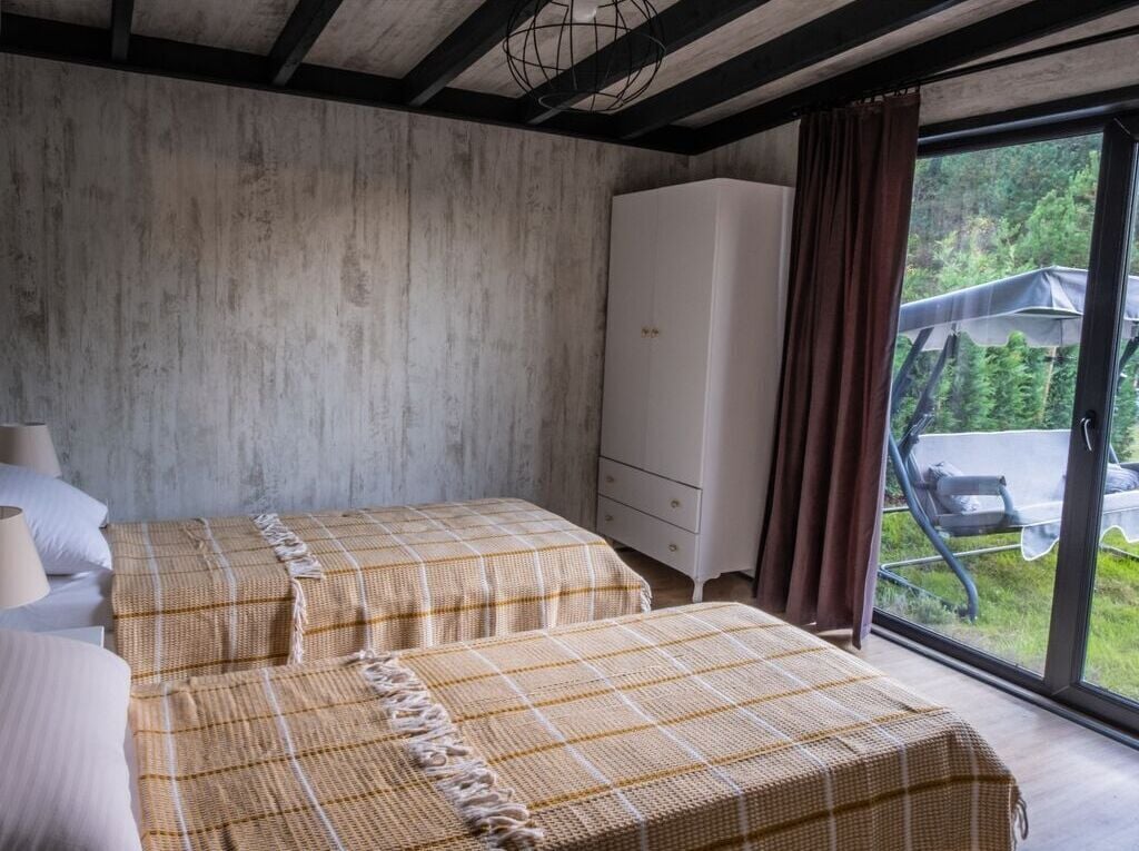 A bedroom with two beds, a wardrobe, and a view of the outdoors through a large window.