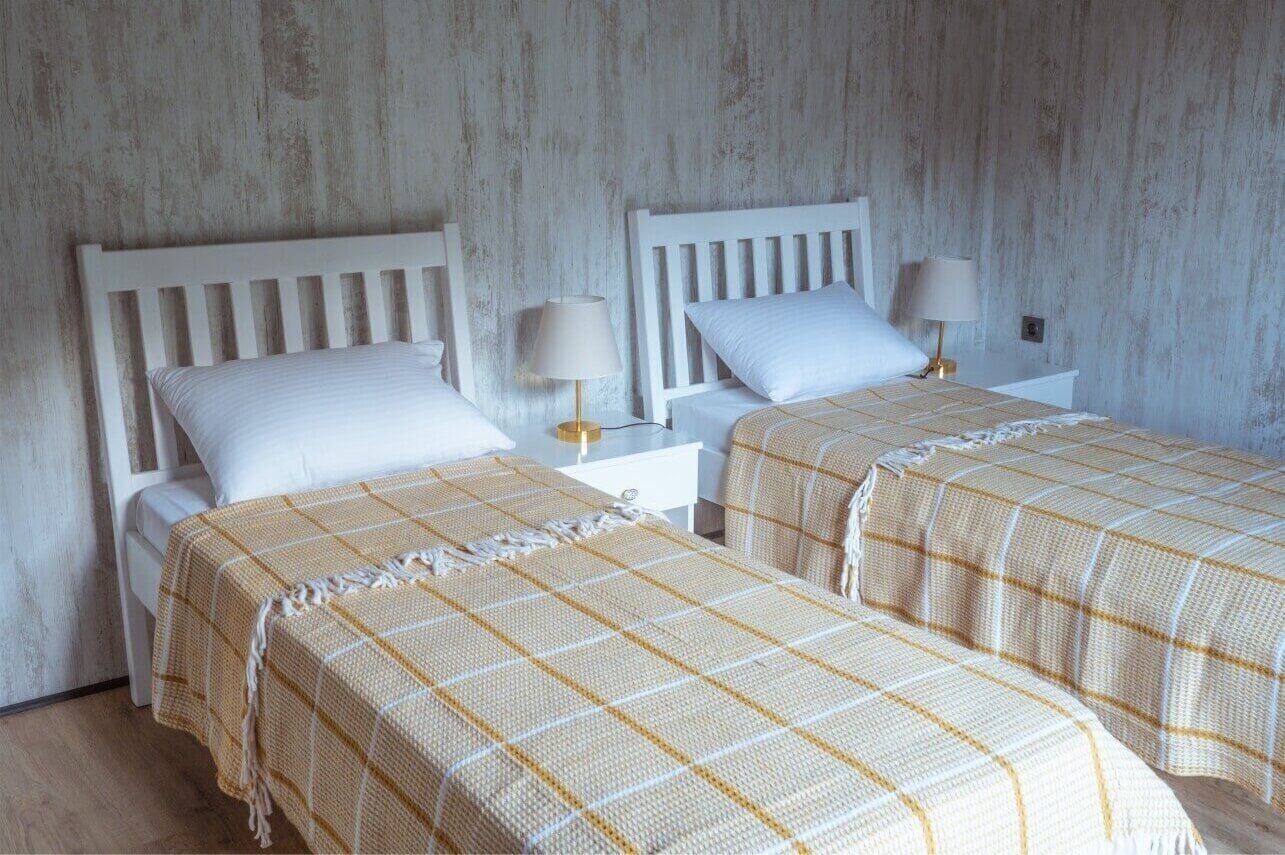 Una habitación con dos camas, cada una con cabecero blanco y un cojín a juego. Hay mesitas de noche con lámparas y una pequeña mesa entre las camas.