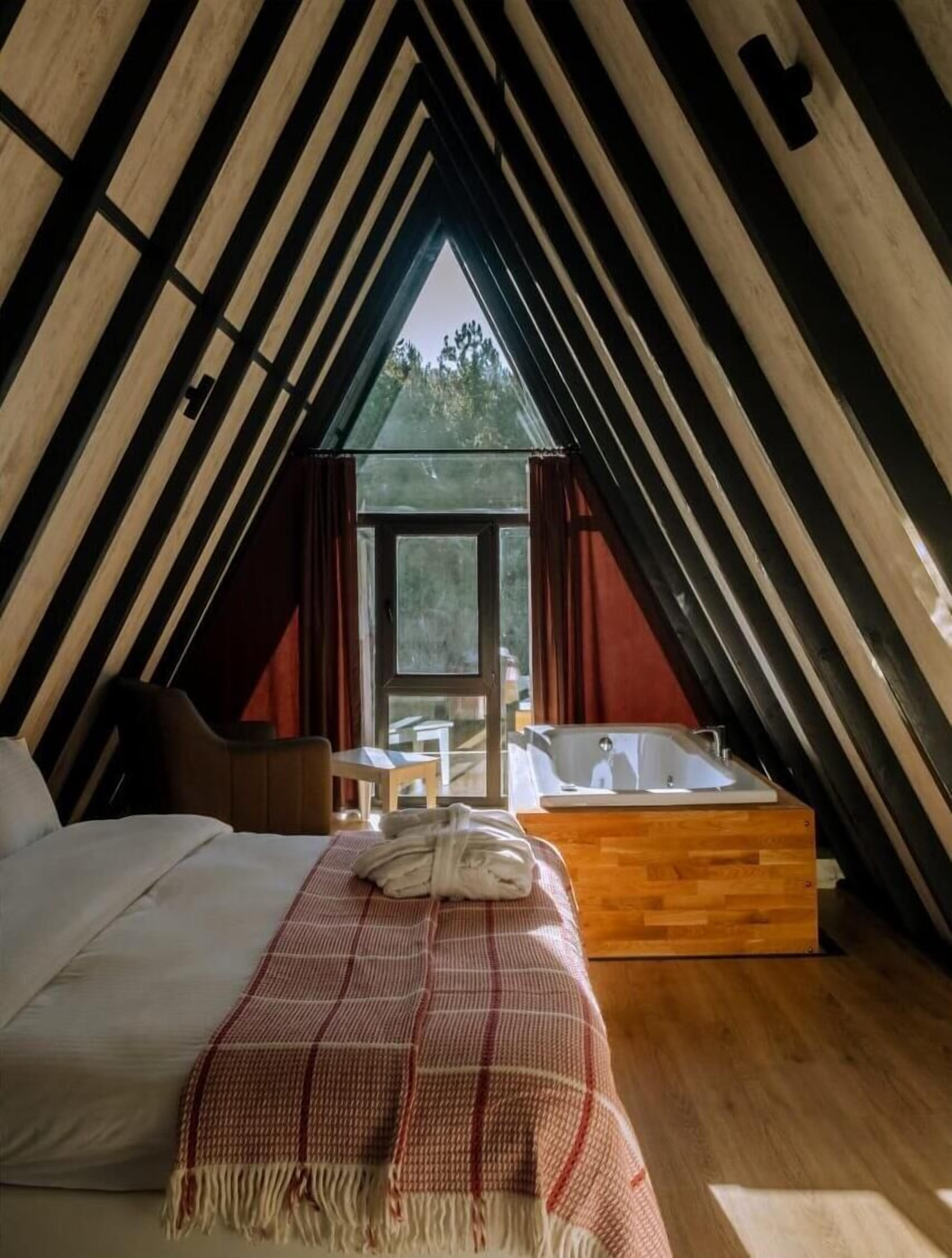 A cozy attic bedroom with a bed, a wooden bench, a small table, and a bathtub.