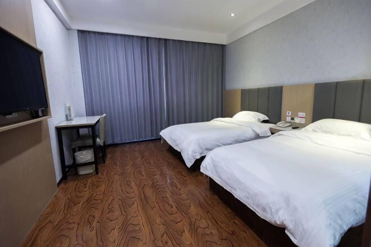 A hotel room with two beds, a desk, a TV, and a curtain.