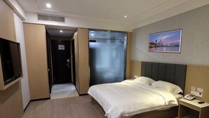 A hotel room with a bed, a TV, a wardrobe, a door, and a painting on the wall. - GreenTree Shell Hotel (Yantai University Yingchun Street) (Yantai)