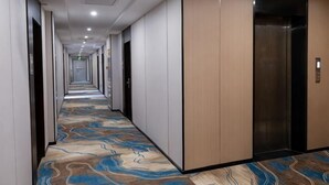 A hotel corridor with a patterned carpet, wooden panel walls, and an elevator. - GreenTree Shell Hotel (Yantai University Yingchun Street) (Yantai)