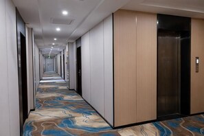 A hotel corridor with a patterned carpet, wooden panel walls, and an elevator. - GreenTree Shell Hotel (Yantai University Yingchun Street) (Yantai)