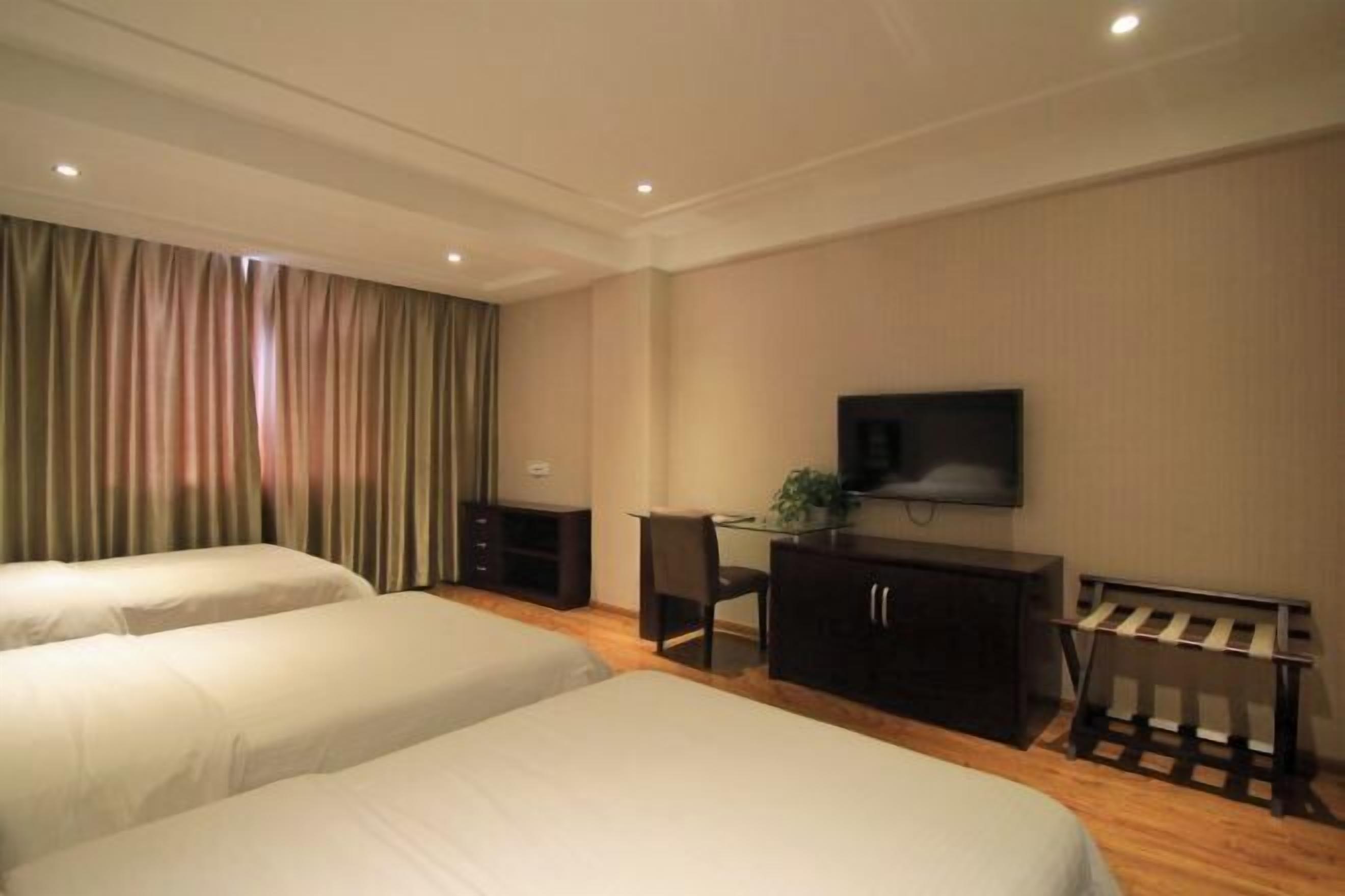 A hotel room with two beds, a desk, a chair, a TV, and a small table with a plant.