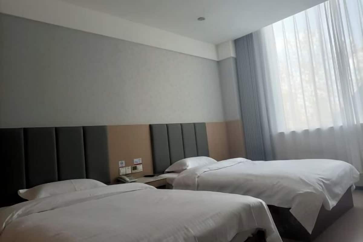 A hotel room with two beds, a headboard, a nightstand, and a window with curtains.
