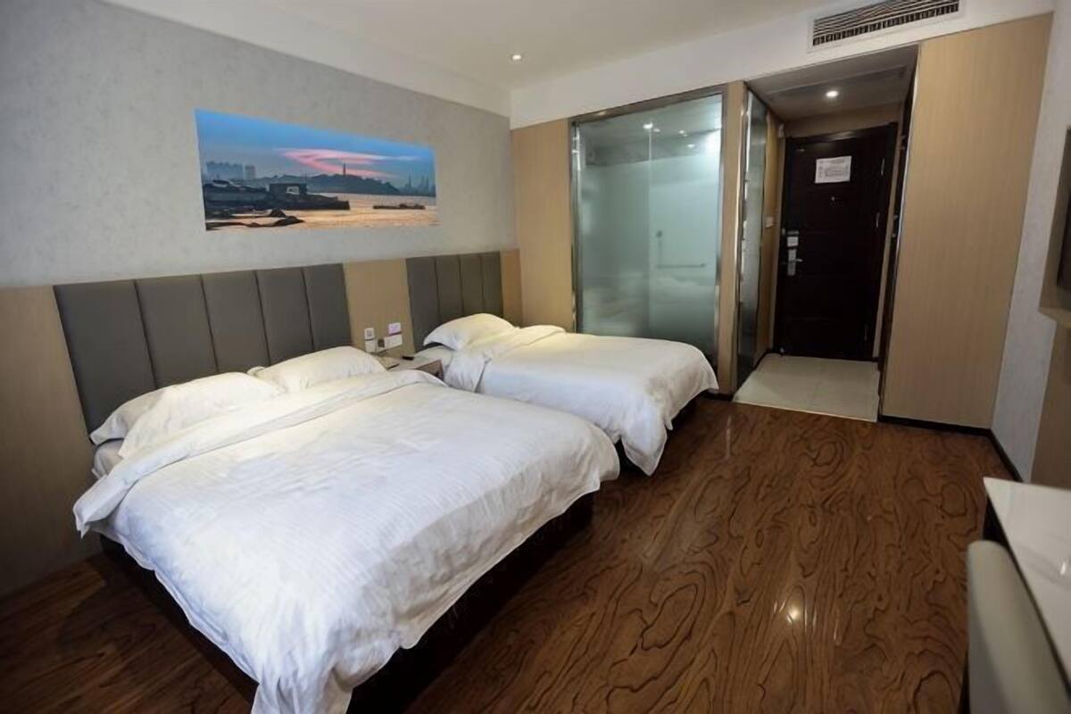 A hotel room with two beds, a cityscape painting, a wooden floor, and a door leading to a bathroom.