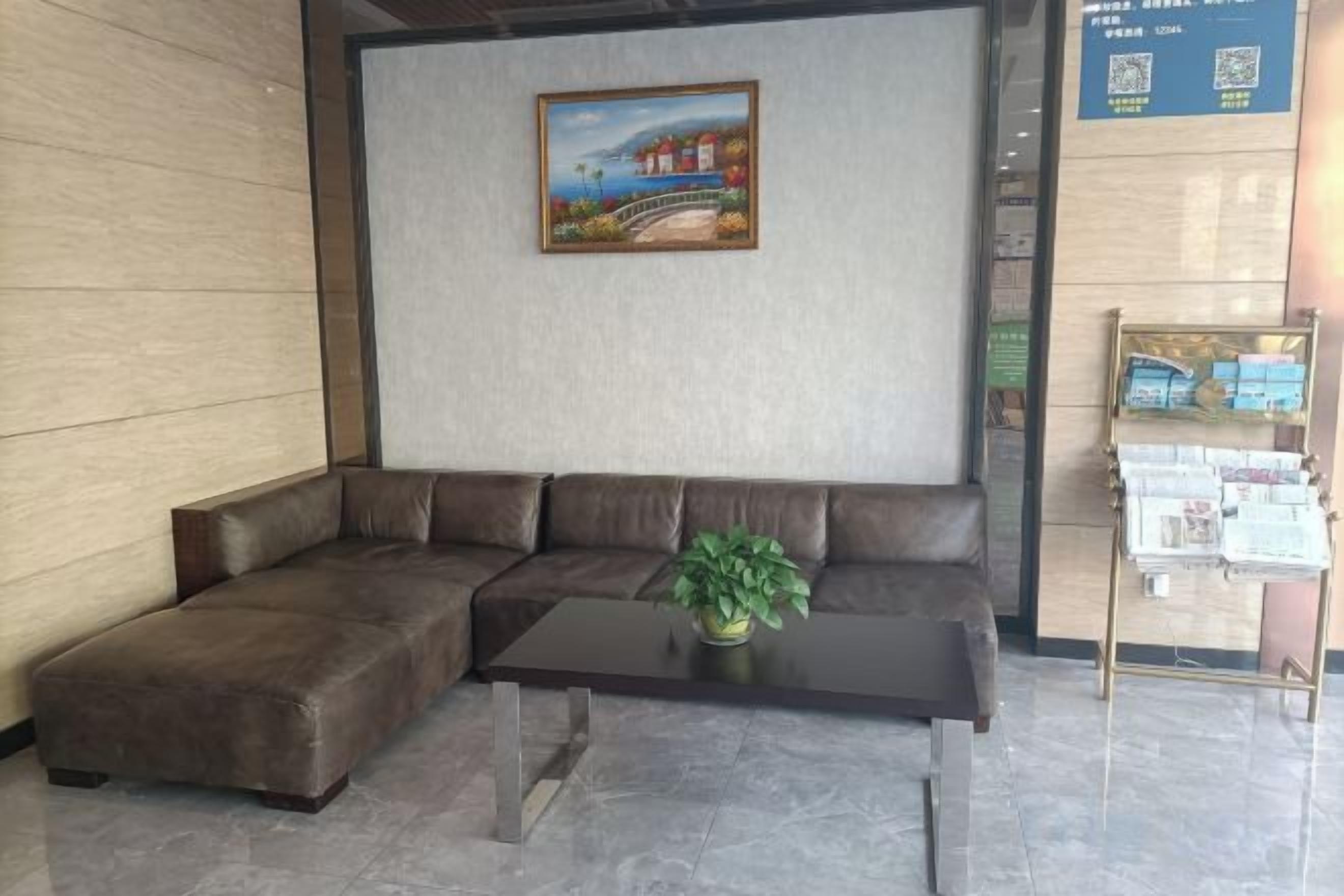 Un hall d’entrée avec un canapé d’angle, une table basse et une petite plante. Un tableau est accroché au mur, et un présentoir contient des brochures.