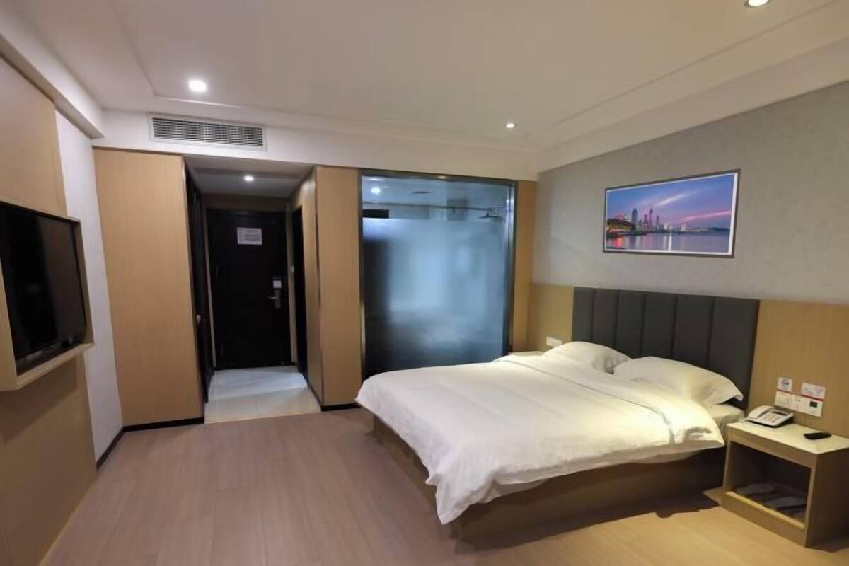 A hotel room with a bed, a TV, a painting, and a door leading to another room.