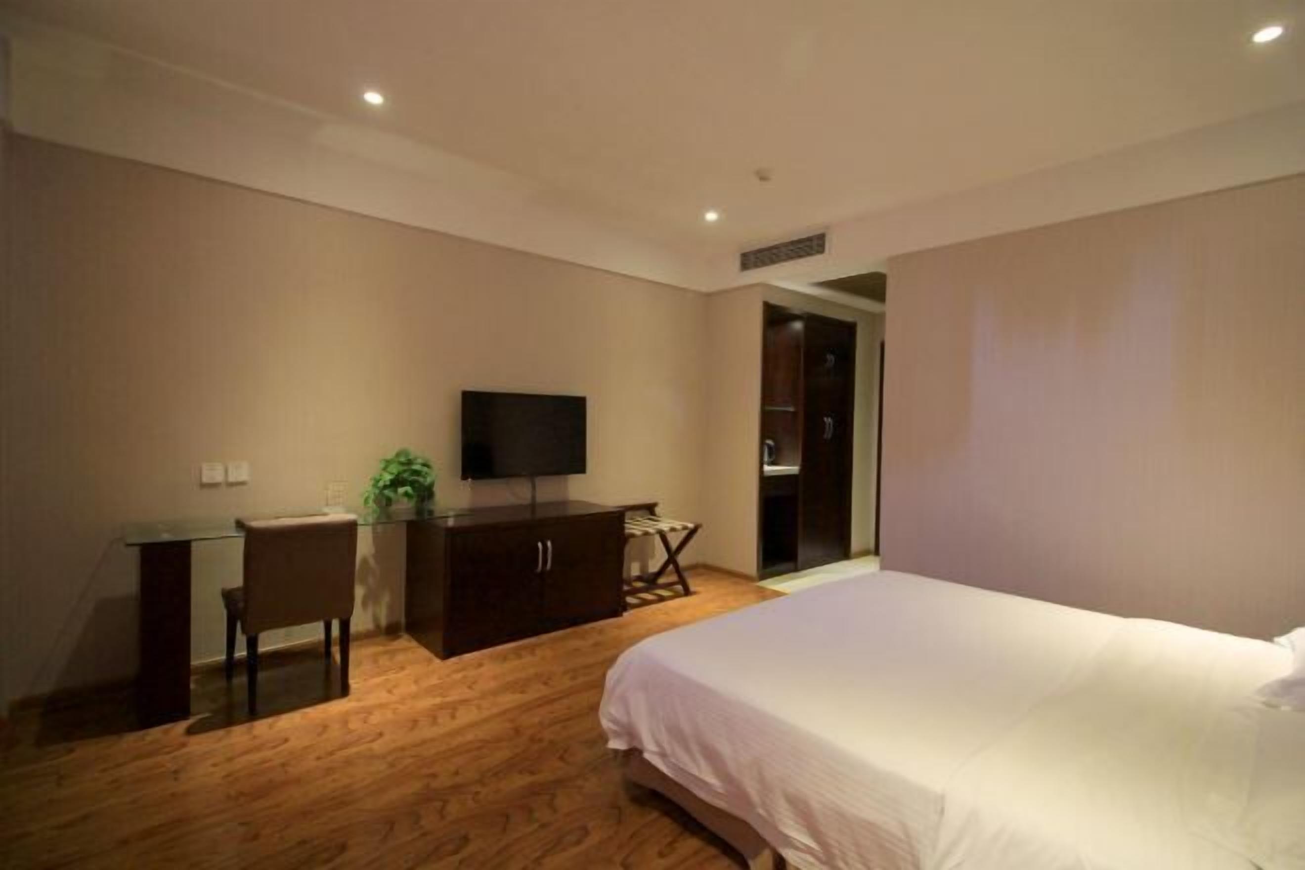 A bedroom with a bed, a desk, a chair, a television, and a wardrobe.