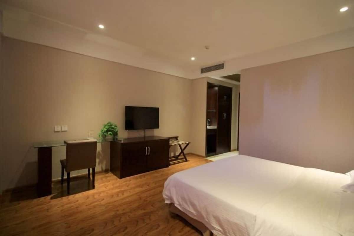 A bedroom with a bed, a desk, a chair, a television, and a wardrobe.
