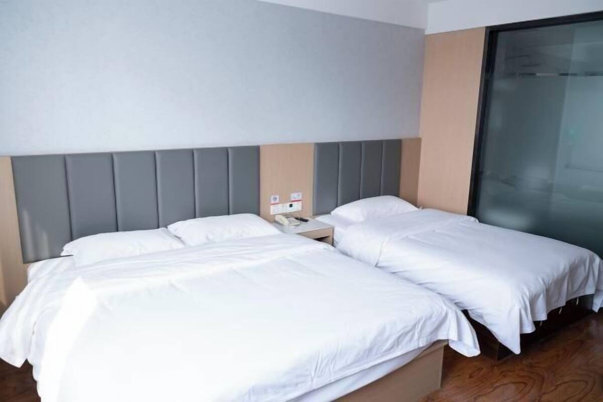 A hotel room with two single beds, a wooden floor, a grey headboard, and a glass door.