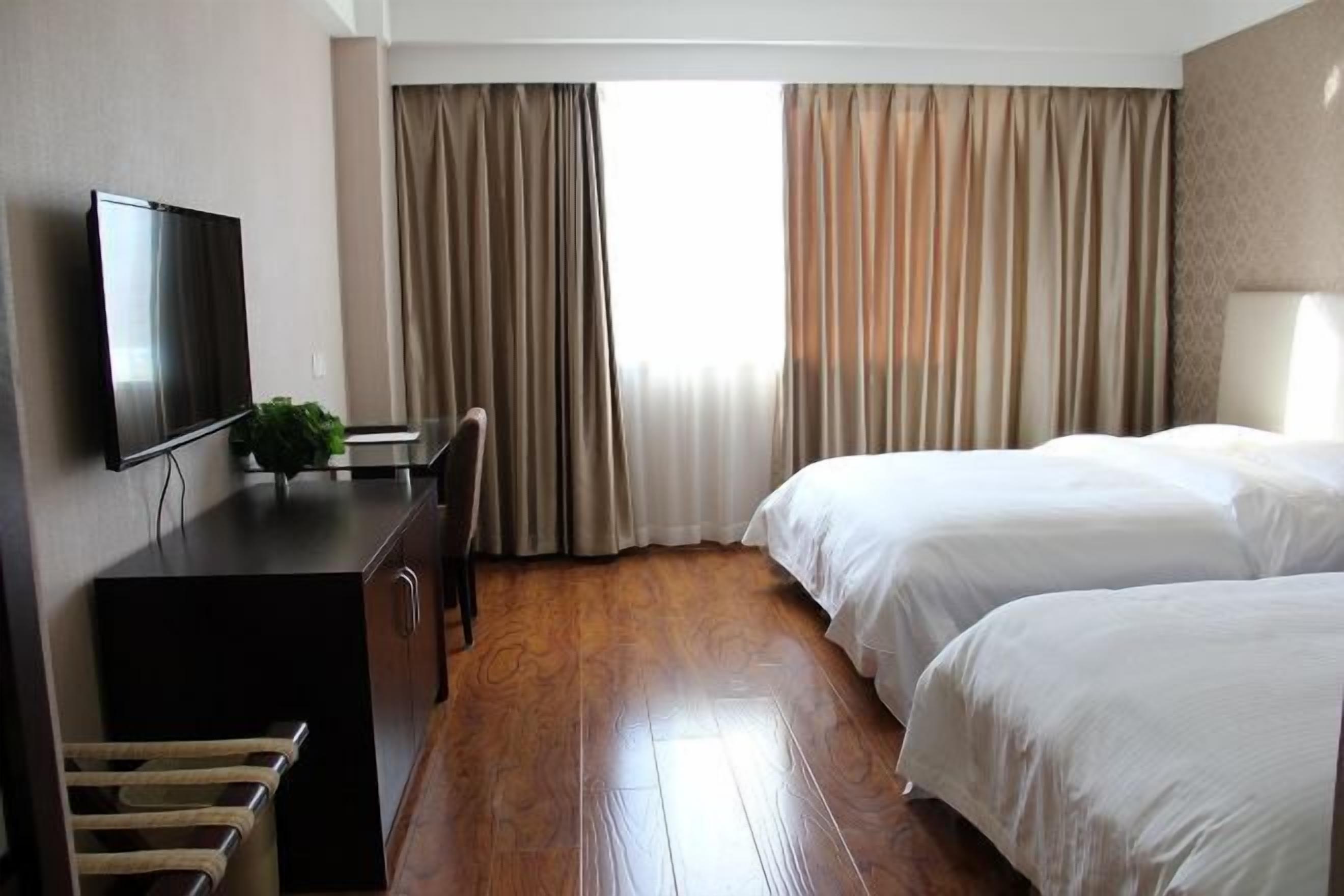 A hotel room with a bed, a desk, a TV, and curtains.