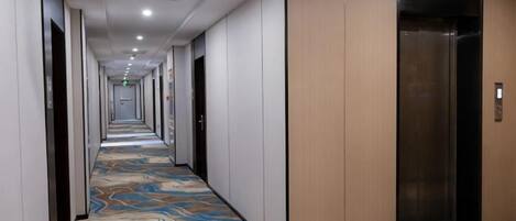 A hotel corridor with a patterned carpet, doors, and an elevator.