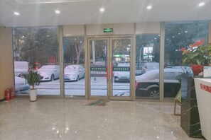 A hotel lobby with a reception desk, a potted plant, and a view of the street outside. - GreenTree Shell Hotel (Yantai University Yingchun Street) (Yantai)