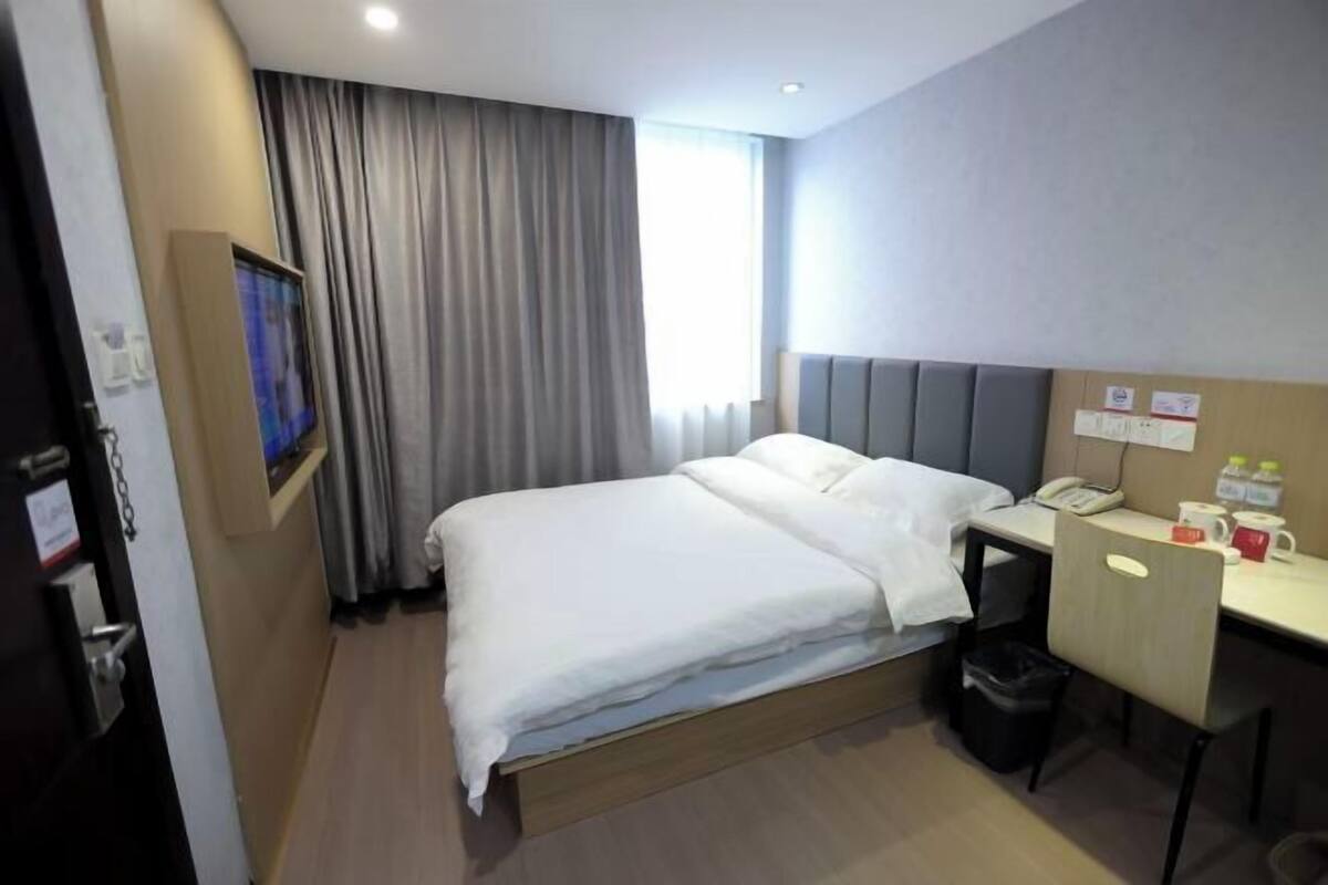 A hotel room with a bed, a desk, a chair, a TV, and a window with curtains.
