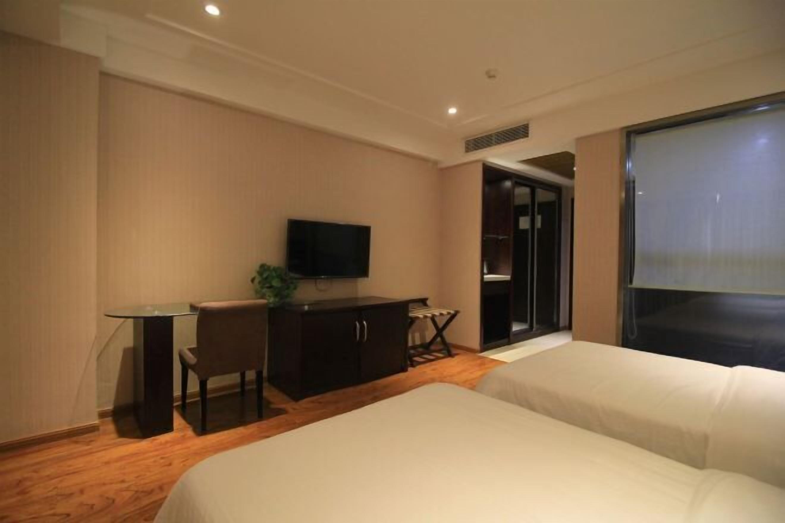 Ein Hotelzimmer mit einem Bett, einem Schreibtisch mit Stuhl, einem Fernseher und einer Schiebetür zu einem Badezimmer.