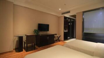 A hotel room with a bed, a desk with a chair, a television, and a sliding door leading to a bathroom.