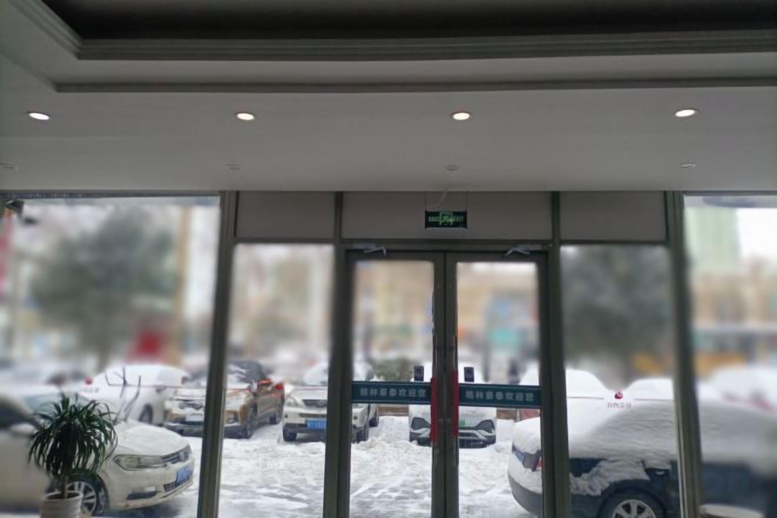Entrada de hotel com porta de vidro, uma placa acima da porta e vista de carros estacionados.
