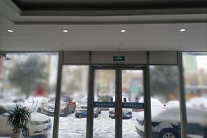 Entrada de hotel com porta de vidro, uma placa acima da porta e vista de carros estacionados.