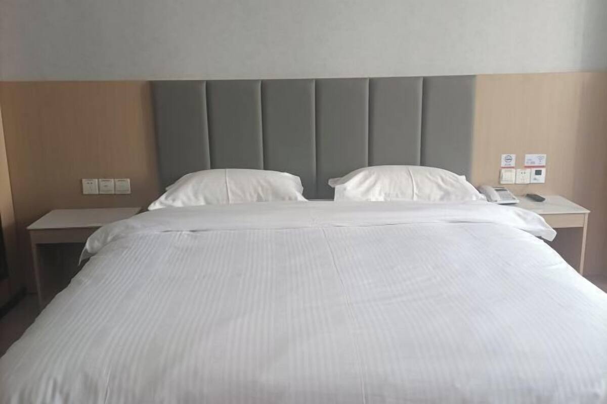 A hotel room with a large bed, two bedside tables, and a headboard with vertical panels.